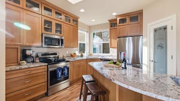 A modern kitchen with wooden cabinets, a granite countertop, stainless steel appliances, and a large island with stools.
