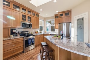 A modern kitchen with wooden cabinets, a granite countertop, stainless steel appliances, and a large island with stools.