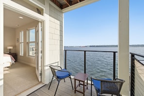 A balcony with a view of the water, a chair, a table, and a bedroom with a bed and nightstand. - Puget Sound waterfront · Rainier · fireplace (Tacoma)