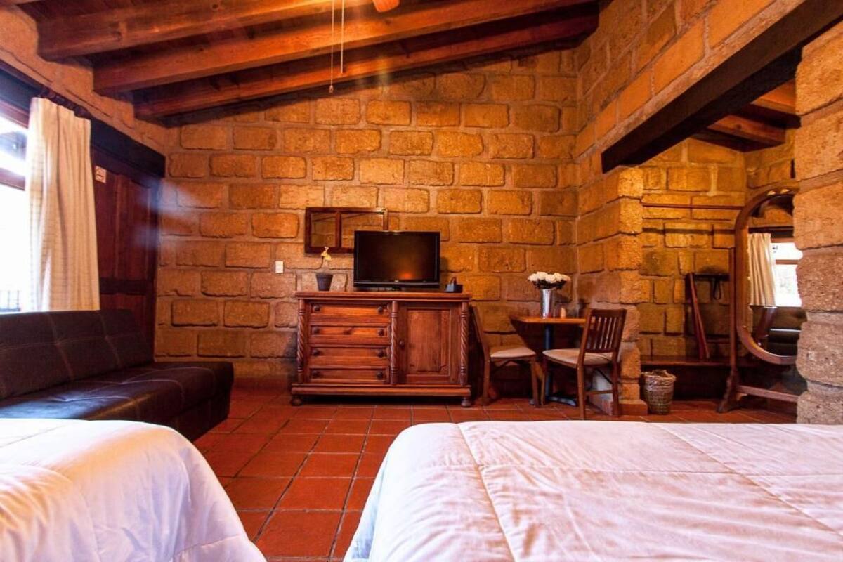 A room with a brick wall, wooden furniture, a television, and a bed.