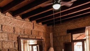 Una habitación rústica con cama, una mesita, ventilador de techo y paredes de piedra.