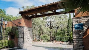 Una entrada protegida por un muro de piedra, una reja metálica y una estructura de pérgola.