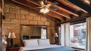 Un dormitorio con pared de piedra, cama, ventilador de techo y ventana con cortinas.
