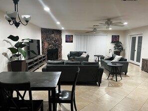 Ein modernes Wohnzimmer mit Kamin aus Stein, einem Essbereich mit Tisch und Stühlen sowie einem Deckenventilator.