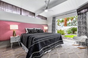 Une chambre à coucher avec un lit, une table de chevet, une lampe et une vue sur l’extérieur.