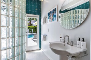 Une salle de bain avec un grand lavabo, un miroir et une porte en verre donnant sur l’espace piscine.