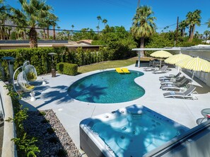Une piscine avec un jacuzzi, des chaises longues et des parasols.