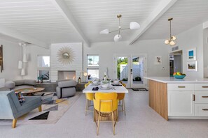 Eine moderne Küche mit weißen Schränken, ein Essbereich mit gelben Stühlen und ein Wohnzimmer mit grauem Sofa.