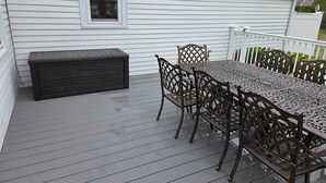 A deck with a table and chairs, a bench, and a house in the background. - A quintessential Cape Cod family home in Dennis Port (Dennis)
