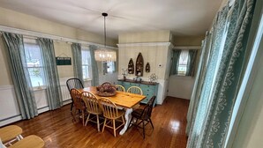A dining area with a wooden table and chairs, a chandelier, and a kitchen area with cabinets and decorative items. - A quintessential Cape Cod family home in Dennis Port (Dennis)