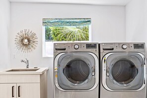 A laundry room with two front-loading washers, a sink, and a decorative wall piece. - Casa Del Solstice - Midcentury Pool & Spa Retreat (Palm Springs)
