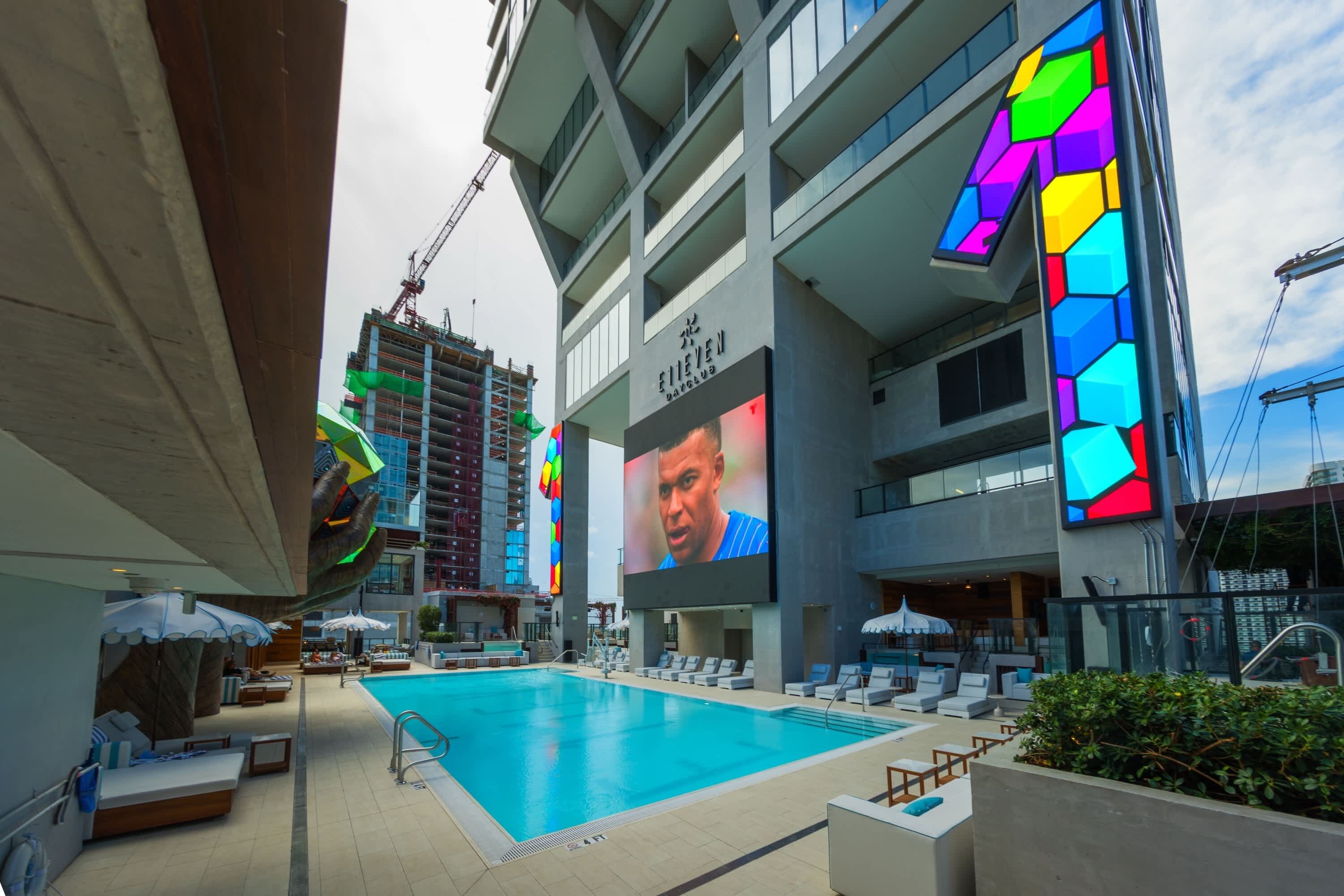 Un hotel con piscina, mobiliario exterior y un gran anuncio digital.
