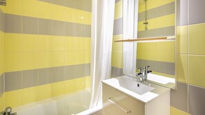 A bathroom with yellow and gray tiles, a white bathtub, a sink with a mirror, and a showerhead. - Alpine Studio in Central Setting (Les Deux Alpes)