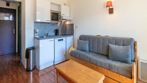 A compact kitchenette with a microwave, coffee maker, and a small refrigerator. There is a grey sofa with cushions and a wooden table in the living area. - Alpine Studio in Central Setting (Les Deux Alpes)