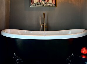 A modern bathroom with a freestanding bathtub, a gold faucet, and a decorative wall piece. - Eclectic Cabin/House - Walk to Ghost Town - Minutes from Big Bend National Park (Terlingua)