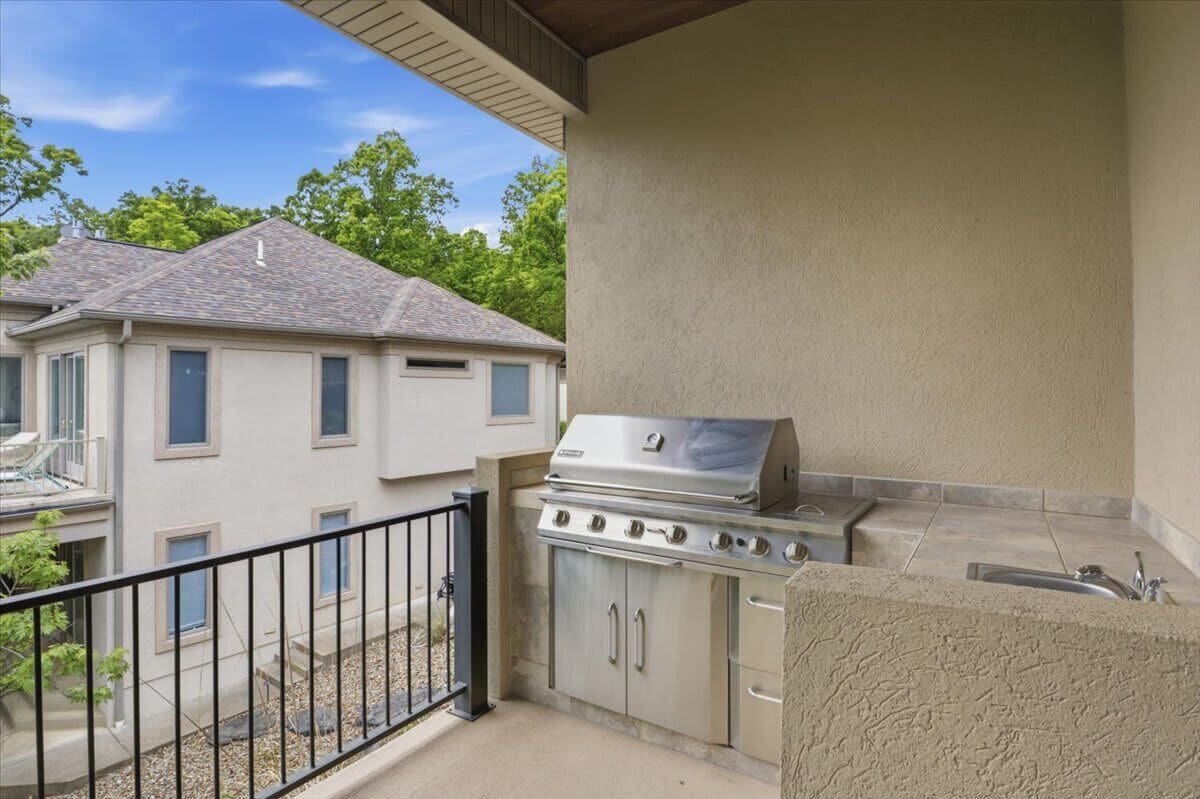 A balcony with a barbecue grill, a sink, and a view of neighboring houses.