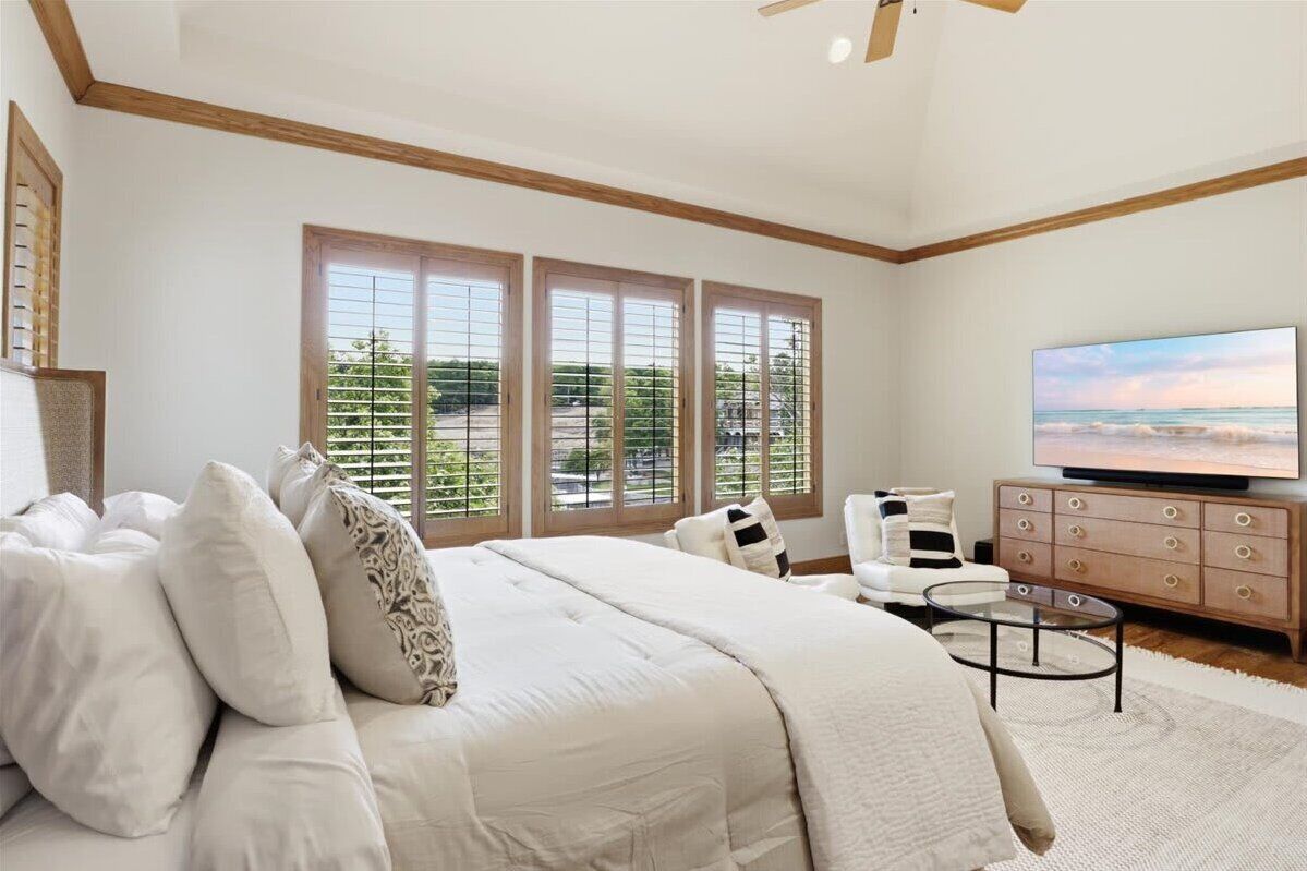 A bedroom with a large bed, a television, a sofa, and a window with blinds.