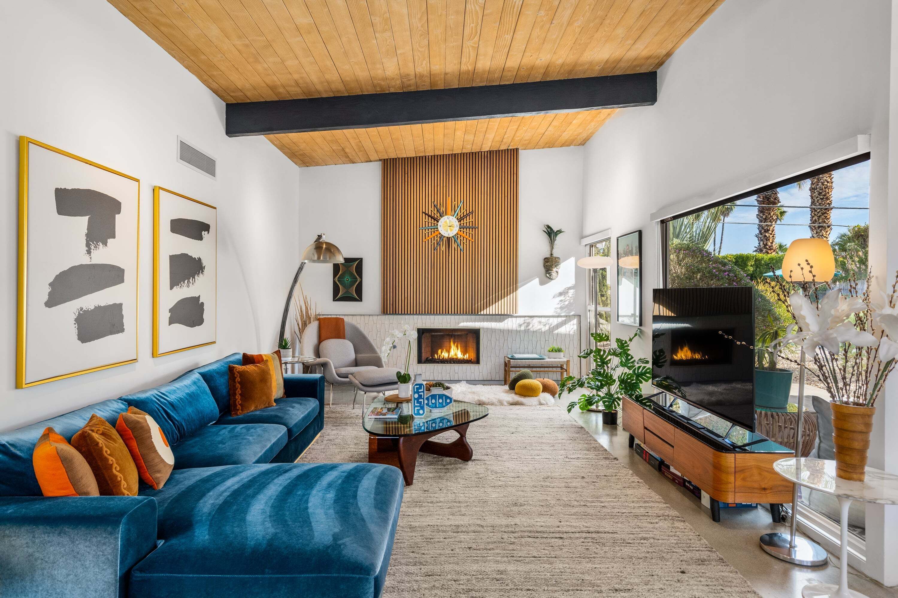A modern living room with a blue sofa, a fireplace, a TV, and a large window.
