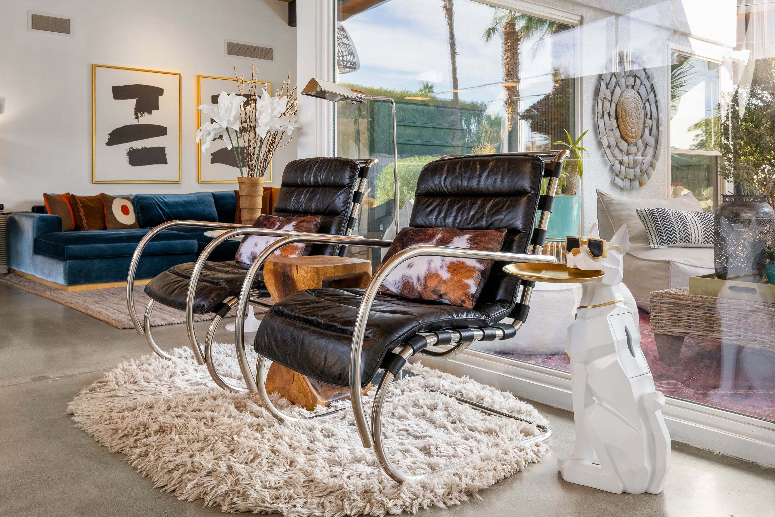 Un salon moderne avec un canapé bleu, deux fauteuils en cuir, une sculpture blanche et des œuvres d’art accrochées aux murs.