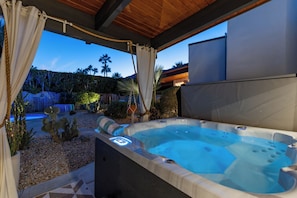 An outdoor hot tub with a wooden ceiling, surrounded by a garden with cacti and a view of palm trees. - Hollywood Hideaway - 1959 Alexander (Palm Springs)