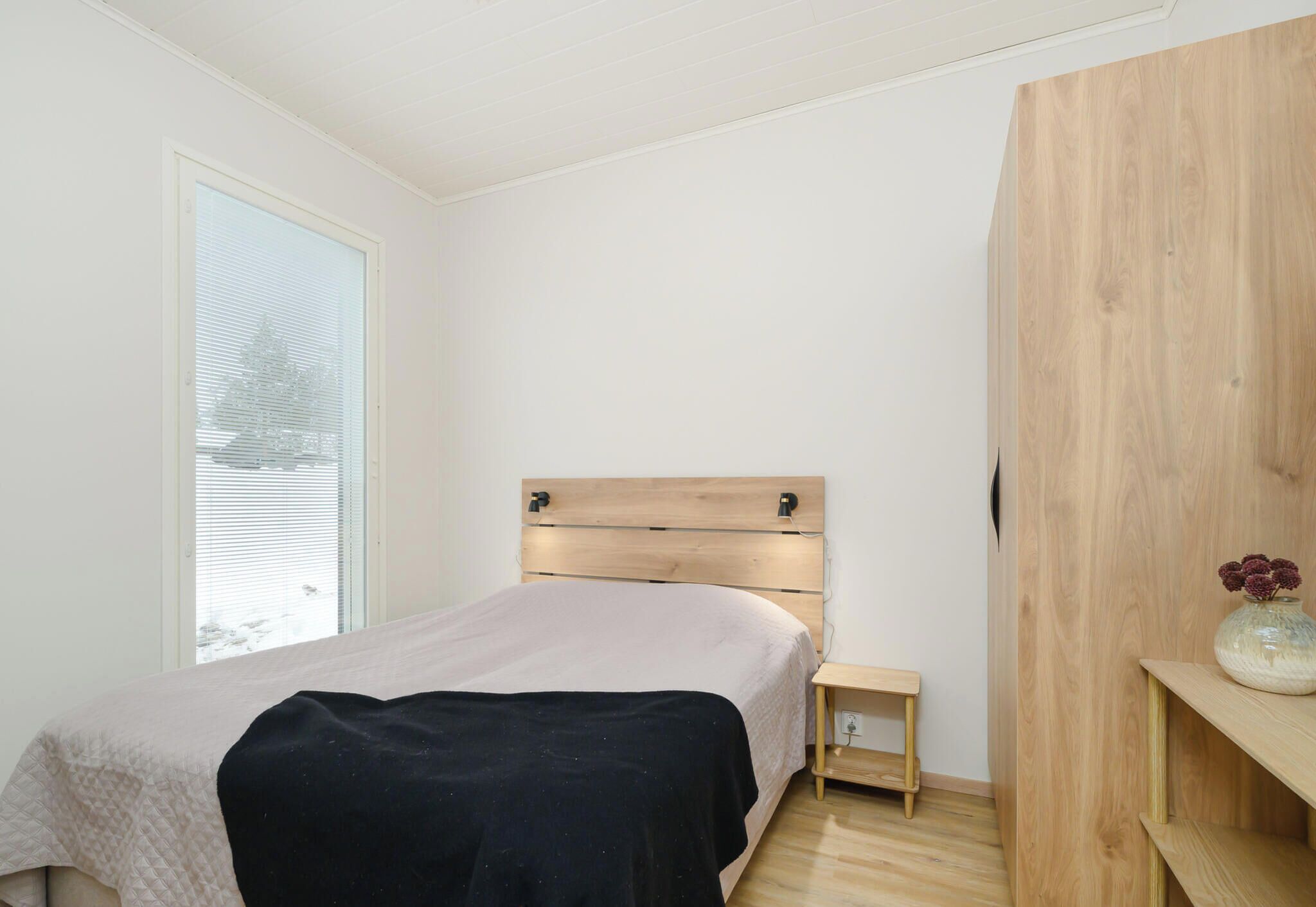 Une chambre à coucher avec un lit, une table de chevet, une armoire en bois et une fenêtre.