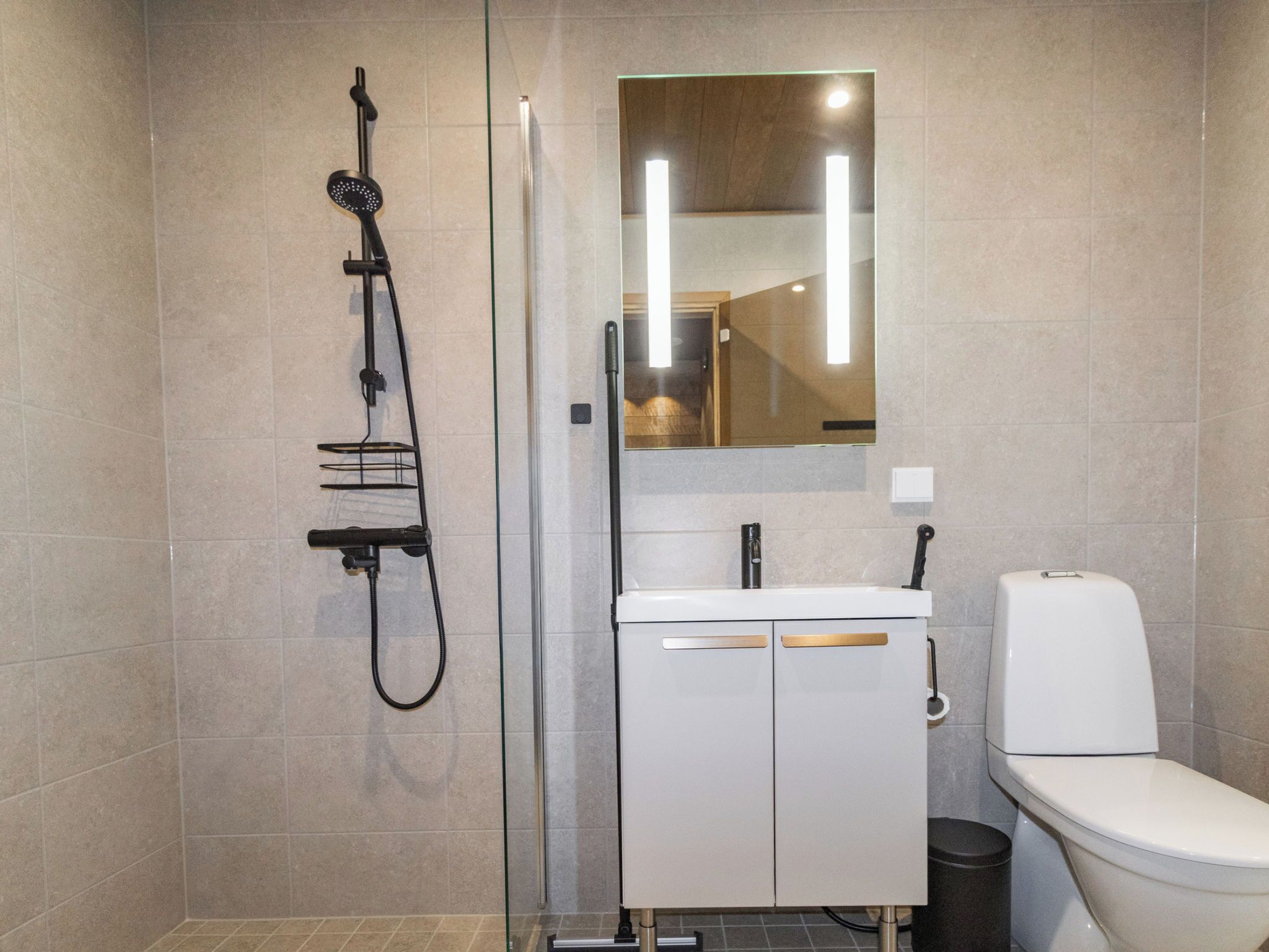 Ein modernes Badezimmer mit Duschkabine aus Glas, einem weißen Waschbecken mit Spiegel darüber und einer Toilette.
