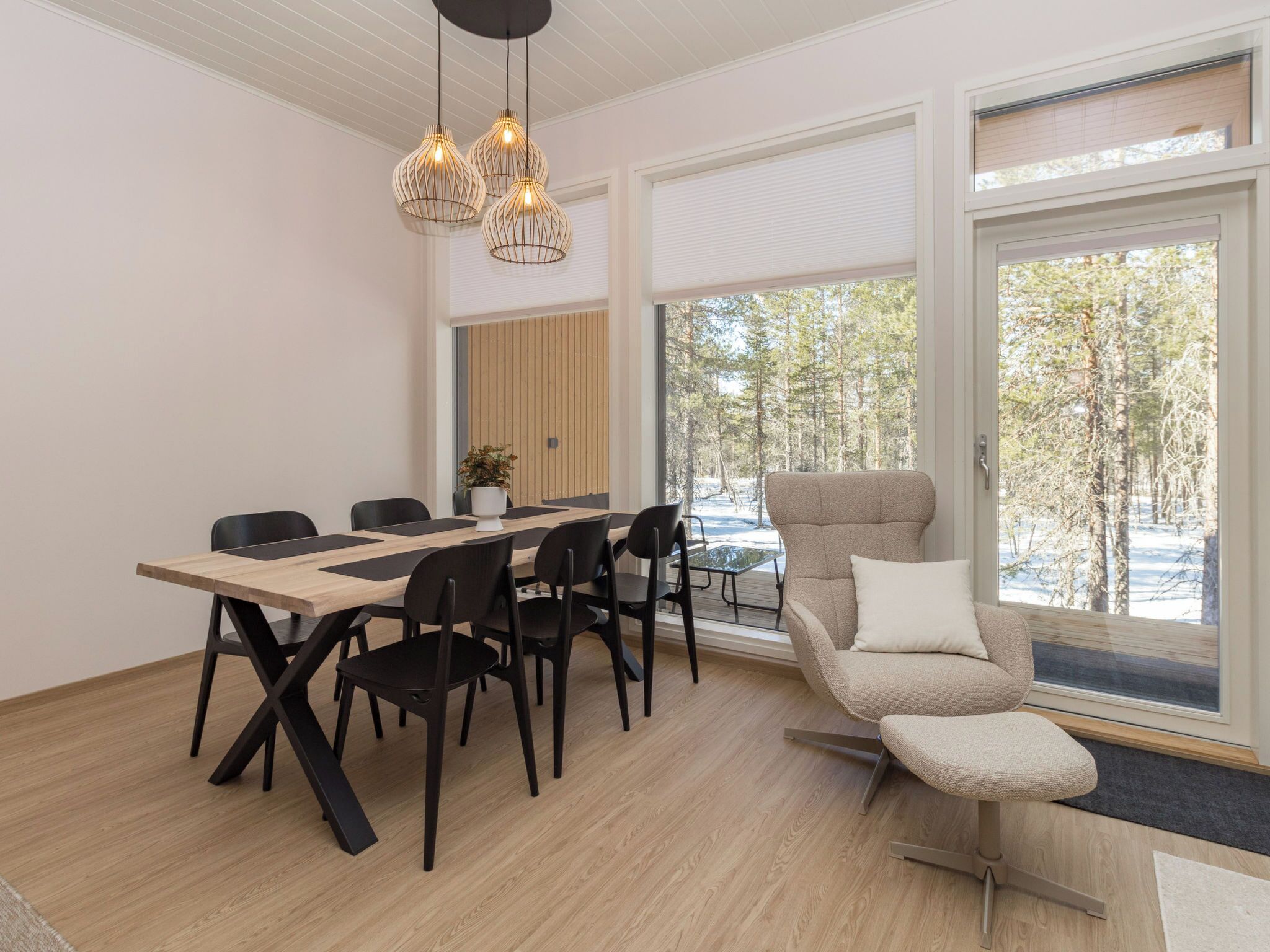 Ein moderner Essbereich mit einem Holztisch, schwarzen Stühlen, einem beige farbenen Sessel und Pendelleuchten.