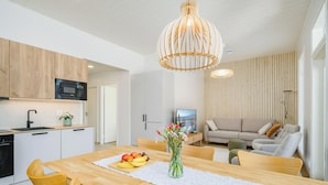 Eine moderne Küche mit Mikrowelle, einem Esstisch mit Obst und Blumen sowie einer Wohnbereits mit Sofa und Fernseher.