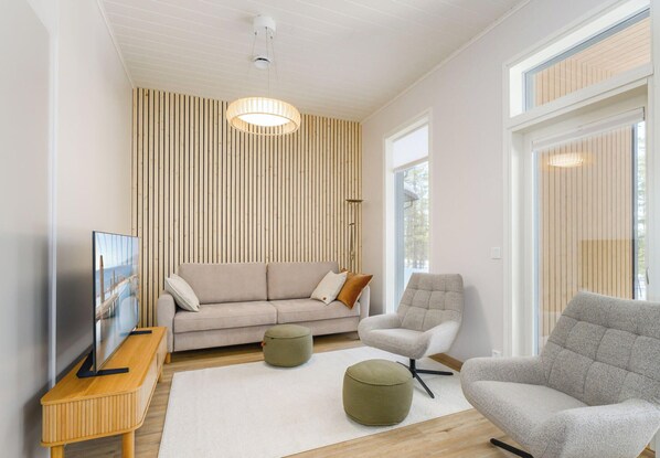 A modern living room with a sofa, armchair, ottoman, TV, and wooden slat wall. - Saariselän aavahelmi c by Interhome (Inari)