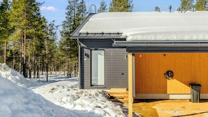 Eine moderne Holzhütte mit einer Holztür, einer Garage und verschneiter Landschaft.