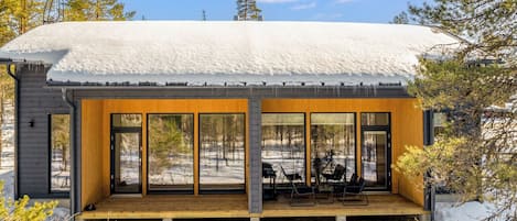 Une cabane moderne dotée d’une terrasse en bois et de grandes fenêtres.