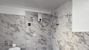 Une salle de bain équipée de toilettes, d’une douche, de murs en marbre et d’un sol carrelé.