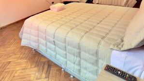 Une chambre d’hôtel avec un grand lit, deux tables de chevet, un téléviseur fixé au mur et un parquet en bois disposé en motif à chevrons.