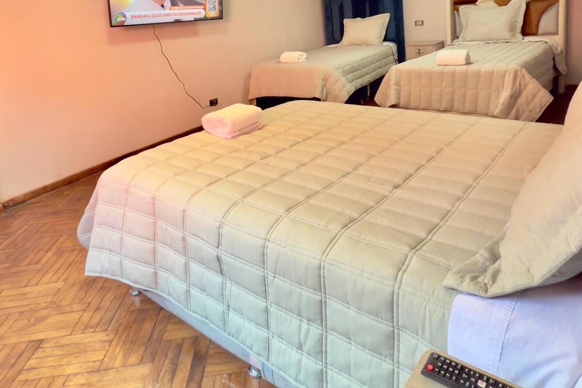 Hotellihuone, jossa on suuri sänky, kaksi yöpöytää, seinälle asennettu televisio ja puinen kalanruotokuviollinen lattia.