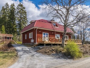 A red wooden house with a red roof, a wooden deck, and a dirt road leading to it. - Virtaan tainio by Interhome (Sysmä)