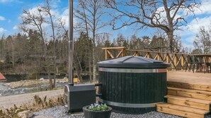 A hot tub with a wooden deck, a metal chimney, and a river in the background. - Virtaan tainio by Interhome (Sysmä)