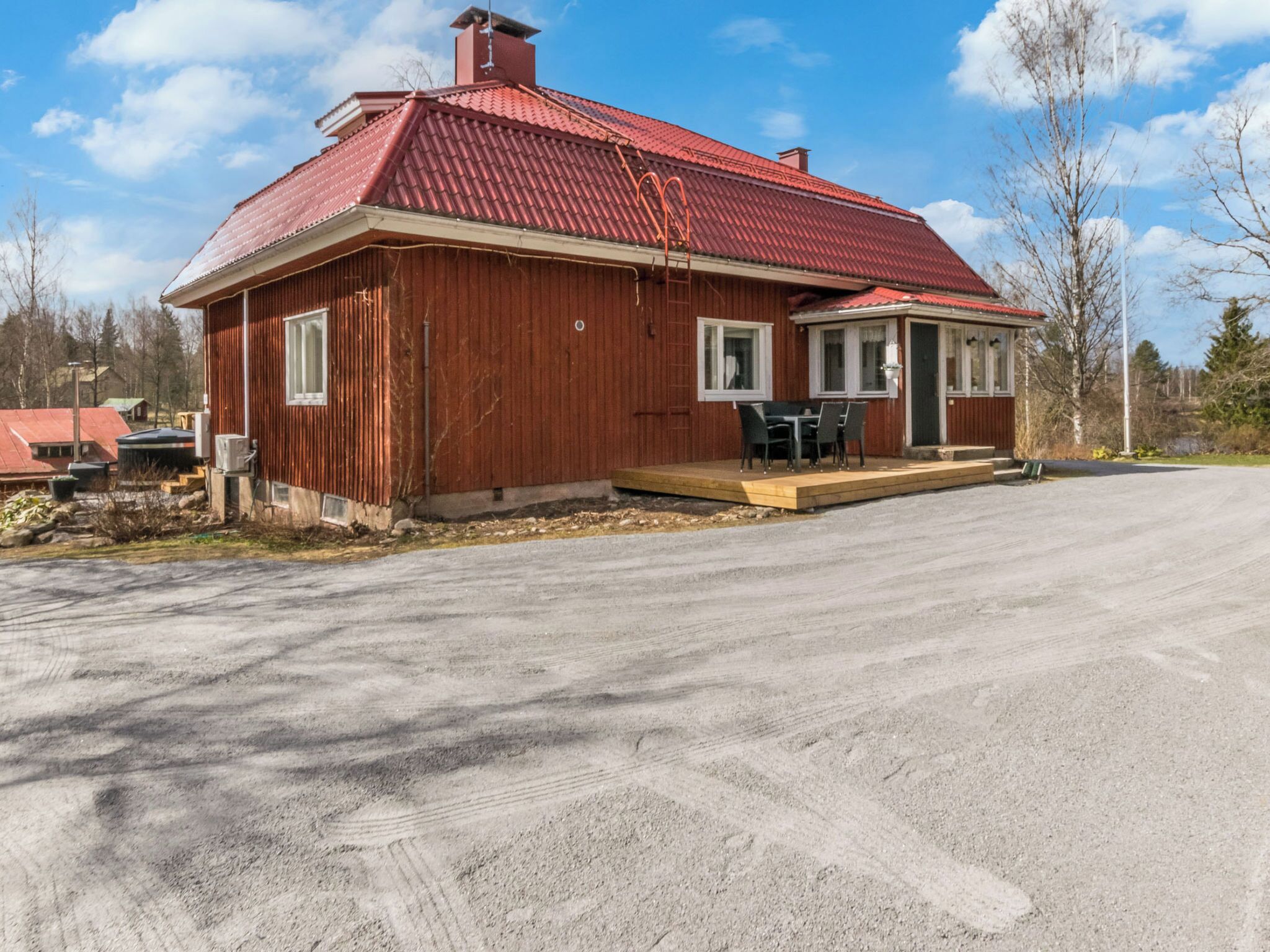 Een rood houten huis met een metalen dak, een veranda met een tafel en stoelen, en een oprit.