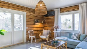 A cozy room with wooden walls, a glass coffee table, a sofa, and a wicker pendant light. - Virtaan tainio by Interhome (Sysmä)