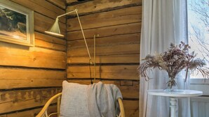 A wooden cabin interior with a wicker chair, a table with a vase of dried flowers, a floor lamp, and a framed picture on the wall. - Virtaan tainio by Interhome (Sysmä)