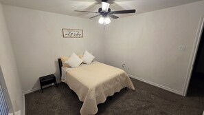 A bedroom with a bed, a nightstand, a ceiling fan, and a wall-mounted light fixture. - Country Retreat - Brand New 3BR/2BA in Poolville, TX (Poolville)