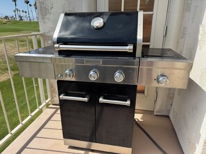 Una parrilla de acero inoxidable para exteriores con cuatro quemadores y un termómetro digital, ubicada en un balcón con vista a un campo de golf.