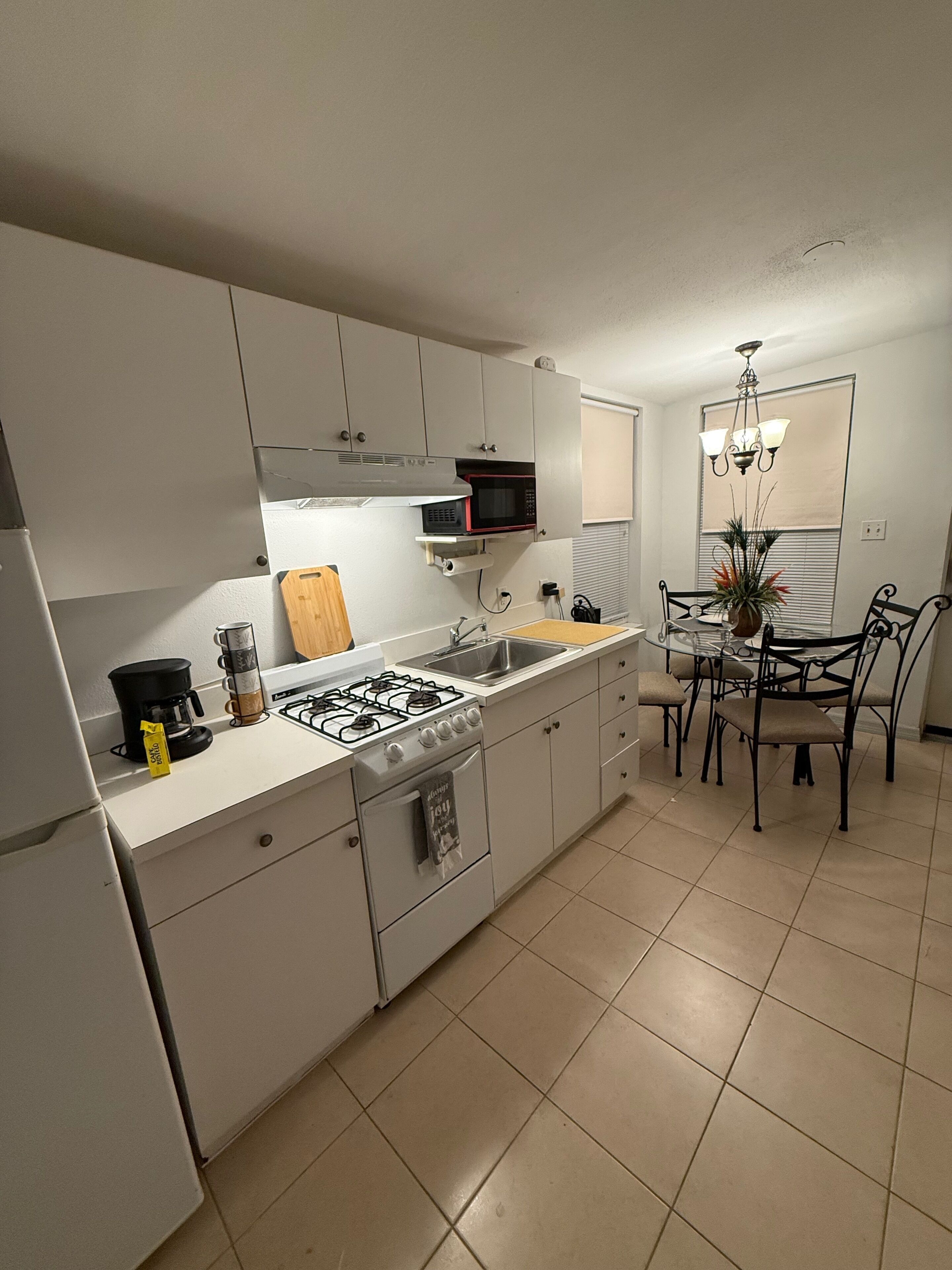 A compact kitchen with white cabinets, a gas stove, a microwave, and a dining area with a table and chairs.