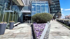Un bâtiment moderne doté d’une façade en verre, d’un espace paysager agrémenté de fleurs et d’un ciel dégagé.