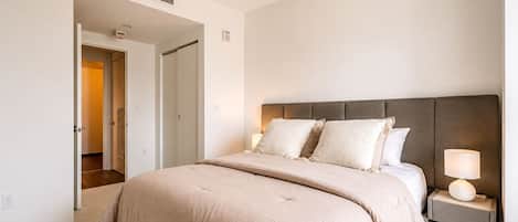 A bedroom with a bed, bedside lamps, and a door leading to another room.