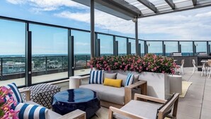 Une terrasse sur le toit dotée d’une balustrade en verre, d’un espace salon extérieur et d’une composition florale.