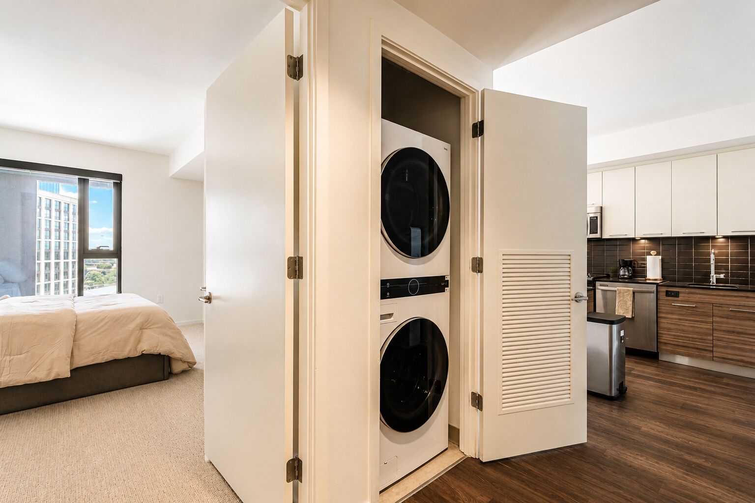 A modern bedroom with a large bed, a view of a cityscape, and a laundry room with two washing machines.