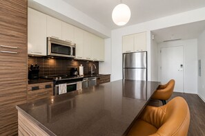 A modern kitchen with stainless steel appliances, a central island, and a seating area with leather chairs. - Modern Luxury Full 1Bedroom Apartment. Pool, Gym & Mall, Metro, & Restaurants (Tysons)