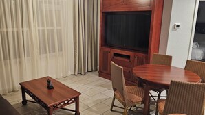 Ein Wohnzimmer mit Fernseher, Couch, Holz-Couchtisch und Korbstühlen.