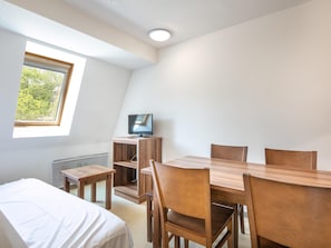 A room with a bed, a dining table with chairs, a TV on a wooden stand, and a window with a view of greenery. - Apartment in Gresse-en-vercors Near Ski-lift (Gresse-en-Vercors)