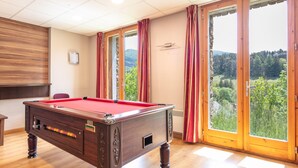 A pool table in a room with wooden flooring, large windows with curtains, and a view of greenery outside. - Apartment in Gresse-en-vercors Near Ski-lift (Gresse-en-Vercors)